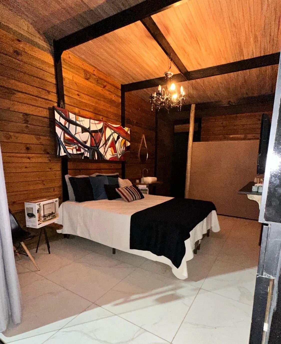 Quarto aconchegante com cama de casal, lustre e acabamento em madeira