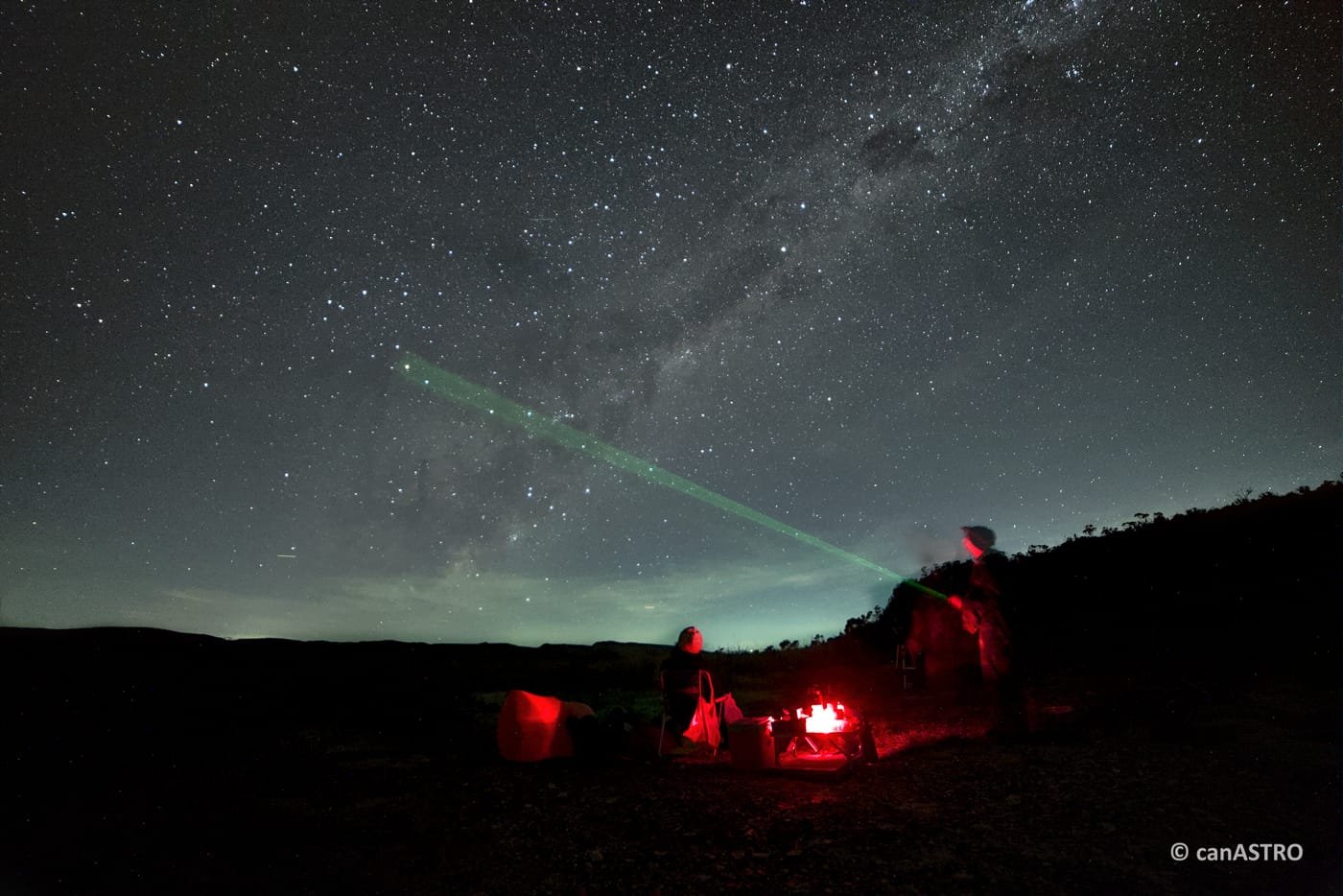 Grupo reunido na serra à noite, sob luz vermelha, enquanto o laser do guia aponta o céu